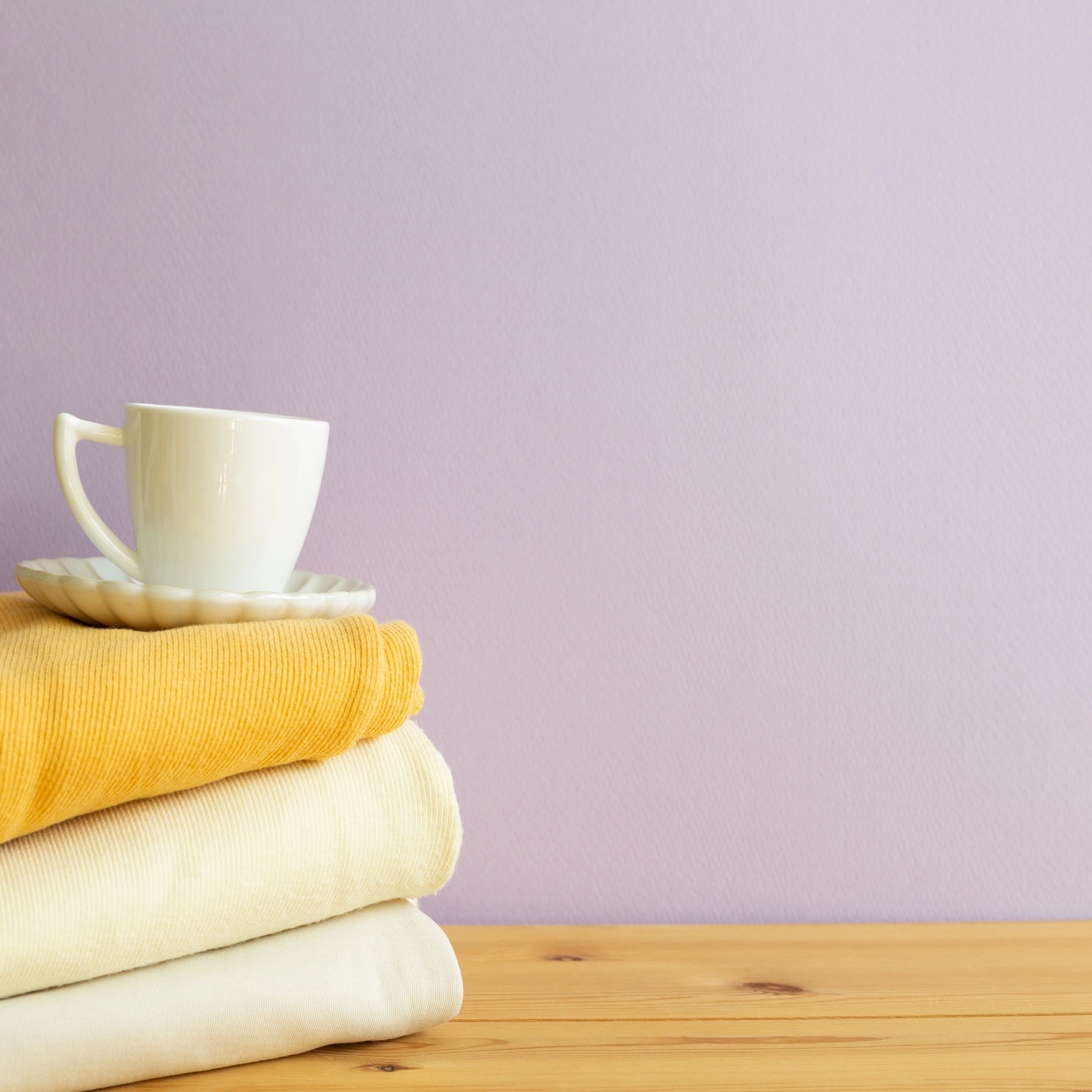 Stack of folded clothes and cup of coffee on wooden table. purple background. copy space